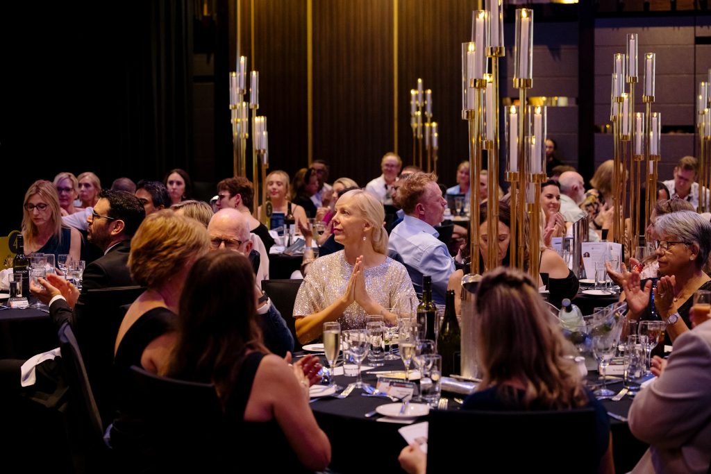 An awards event dinner with many people sitting around tables applauding